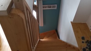 Una escalera de madera con barandilla que lleva a una habitación con pared azul y una ventana con cortinas.