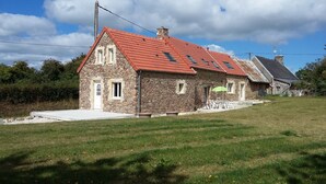 Una casa de piedra con techo rojo, un porche pequeño y un patio cubierto de césped.