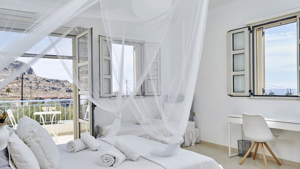 A bedroom with a bed, a desk, and a chair. There is a window with a view of the outside. - Luxury on Rhodes (Lardos)