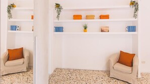 Une pièce aux murs blancs, avec un sol à motifs, deux fauteuils beiges et une étagère blanche contenant des boîtes de rangement orange et une petite plante.