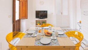 Un coin repas avec une table en bois dressée pour quatre personnes, des chaises jaunes et un téléviseur posé sur un meuble au fond de la pièce.
