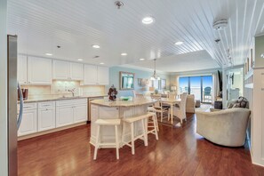 Une cuisine spacieuse avec des meubles blancs, un îlot central doté de tabourets et un coin repas avec une grande chaise.