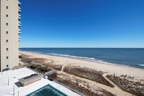 Un grand hôtel avec de nombreuses étages, donnant sur une plage, doté d’une piscine et d’un espace délimité par une clôture.