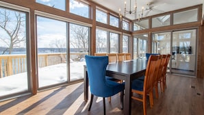 Une salle à manger spacieuse avec de grandes fenêtres, une terrasse en bois et une vue sur un paysage enneigé.