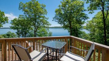 Une terrasse en bois avec une table en verre et deux chaises, donnant sur un lac bordé d’arbres.