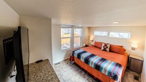 A bedroom with a large bed, two windows, a television, and a small table.