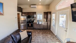 A compact kitchen with dark wooden cabinets, stainless steel appliances, and a window overlooking a balcony.