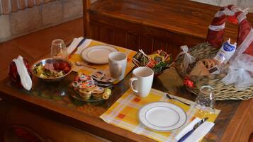 Uma mesa de jantar posta com pratos, uma saladeira de frutas, uma caneca e diversos acompanhamentos.