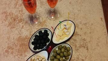 Una mesa con dos vasos de bebida roja, un plato con aceitunas negras, un plato con queso y galletas, un plato con aceitunas verdes y un plato con pistachos.