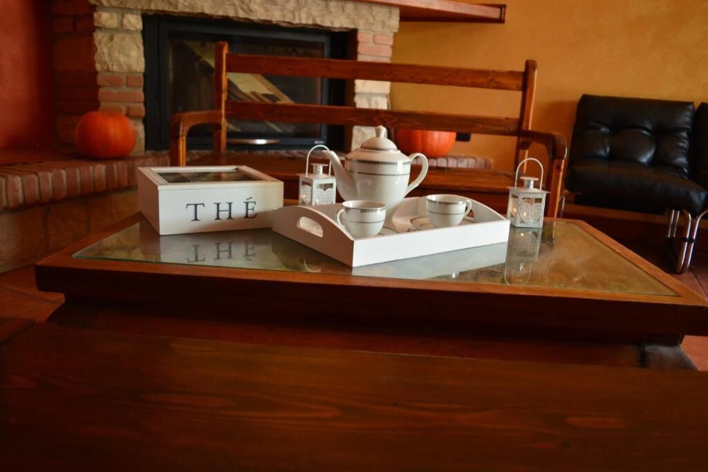 A tray with tea set on a glass table, a fireplace, and a black leather sofa in the background.