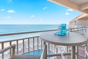 Un balcon avec vue sur l’océan, une table ronde avec un plateau en verre et un espace piscine.