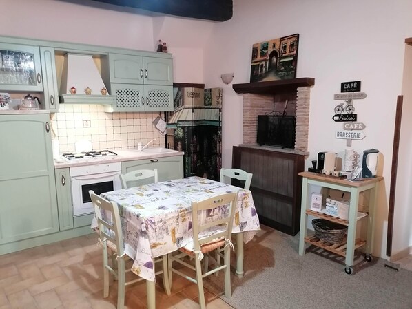 A cozy kitchen with a dining table, light green cabinets, a gas stove, and a brick oven.