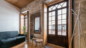 A room with a wooden floor, a black sofa, a small round table, and a large window with a view of the outside. - GuestReady - CastleRock Pub (Live Music) (Porto)