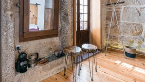 A rustic room with a stone wall, wooden floor, a wooden bench, a coffee machine, and a window with a view of the outside. - GuestReady - CastleRock Pub (Live Music) (Porto)