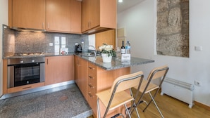 A modern kitchen with wooden cabinets, a granite countertop, a built-in oven, a coffee maker, and a small island with two chairs. - GuestReady - Daisy boutique (Porto)