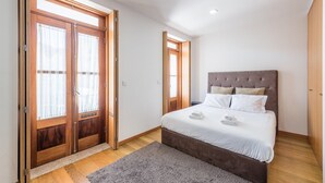 A bedroom with a large bed, wooden wardrobe, and a sliding glass door. - GuestReady - Daisy boutique (Porto)