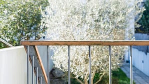 A metal railing with a wooden top, a white wall, and a tree with white blossoms in the background. - GuestReady - Daisy boutique (Porto)