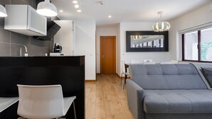 A modern kitchen with a black countertop and white chairs, a grey sofa, and a wooden floor. - GuestReady - Paragon in Porto (Porto)