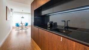A modern kitchen with a black countertop, stainless steel sink, and wooden cabinetry. - GuestReady - Hemisphere Apt (Porto)