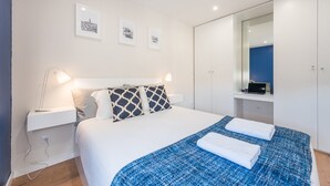 Une chambre d’hôtel moderne avec un lit soigneusement fait, des lampes de chevet, un grand miroir et des œuvres d’art encadrées accrochées au mur.