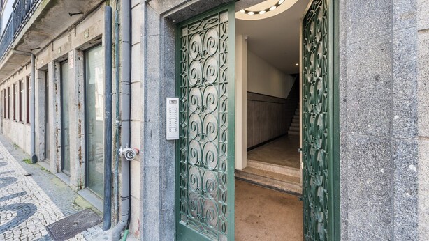 Une entrée d’immeuble avec une porte verte ornée, un clavier pour ouvrir la porte et un escalier visible menant à l’intérieur.