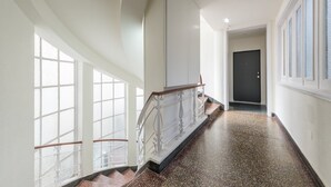 Un intérieur moderne avec un sol en pierre polie, un escalier doté d’une rampe blanche et de grandes fenêtres laissant entrer la lumière naturelle.