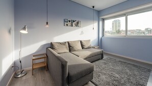 Un salon moderne avec un canapé gris, un lampadaire et une grande fenêtre donnant sur la ville.