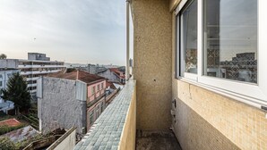 Un balcon étroit doté d’un sol carrelé, une fenêtre offrant une vue sur le paysage urbain et un mur en briques.