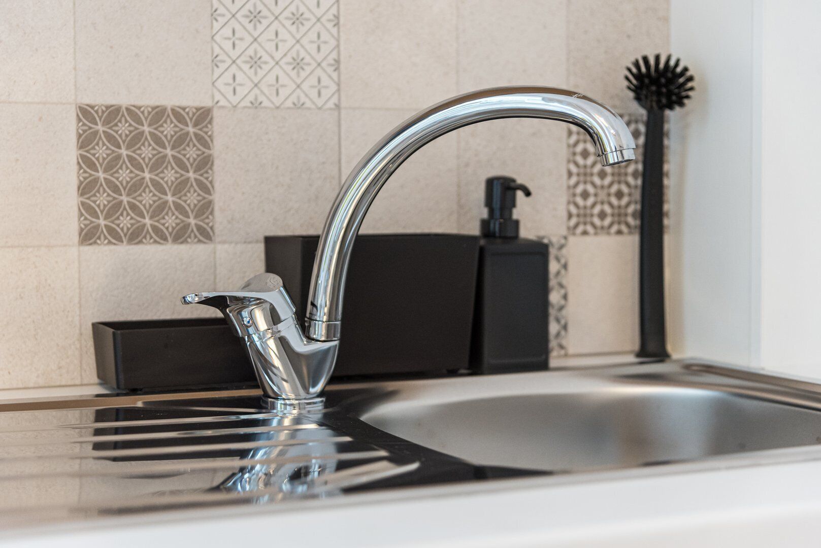 A modern kitchen sink with a chrome faucet, a soap dispenser, and a decorative vase.