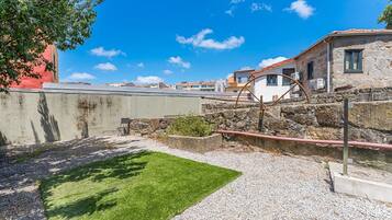 Un patio con césped, un muro de piedra y un edificio con techo de tejas.