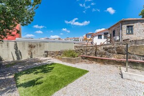 A courtyard with a grassy area, a stone wall, and a building with a tiled roof.