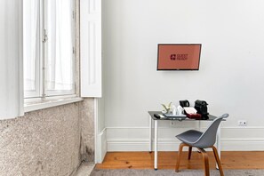 A hotel room with a white wall, a framed 'GUEST READY' sign, a small table with a coffee maker, a chair, and a window with white curtains. - GuestReady - Porto Home 1 (Porto)