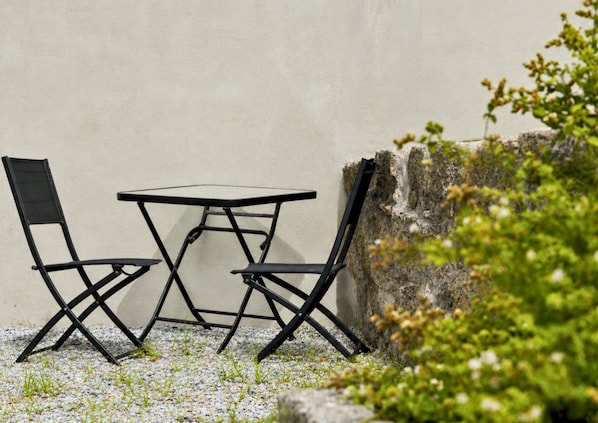A small outdoor seating area with a table and two chairs, positioned against a wall with a rock and greenery. - GuestReady - Porto Home II (with balcony) (Porto)