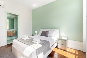 A hotel room with a bed, bedside tables, a nightstand, a bathroom with a mirror, and a green wall.