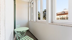 Een hoekzaal met een klein tafeltje en stoelen, een raam met uitzicht op gebouwen, en een deur.