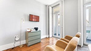 Een moderne kamer met een houten vloer, een grijs kastje, een televisie en een bank.
