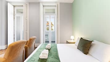 Hotelkamer met een bed, twee stoelen, een tafel, een lamp en uitzicht door een glazen deur.
