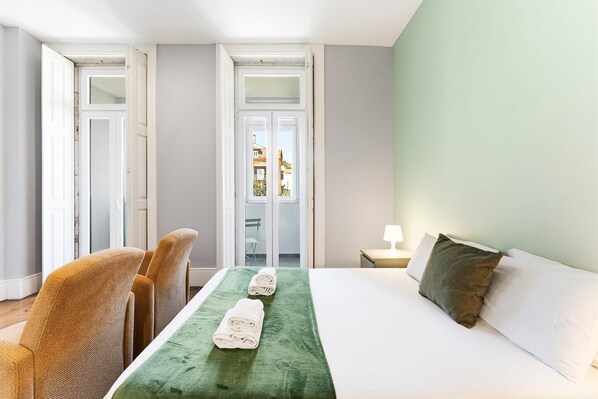 A hotel room with a bed, two chairs, a table, a lamp, and a view through a glass door. - GuestReady - Porto Home IV (Porto)