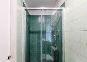 A glass-enclosed shower stall with green tiles, a handheld showerhead, and a wall-mounted faucet.