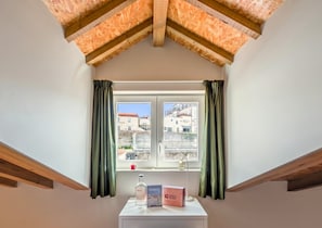 A room with a sloped ceiling, a window with curtains, a small table with a bottle, a book, and a sign.