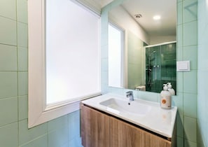 A bathroom with a white sink, wooden vanity, a large mirror, and green tiles.