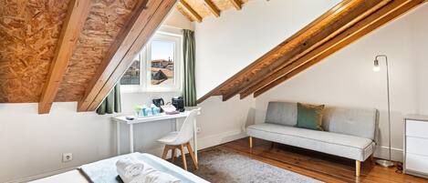 A loft bedroom with a sloped ceiling, a desk, a sofa, and a bed.