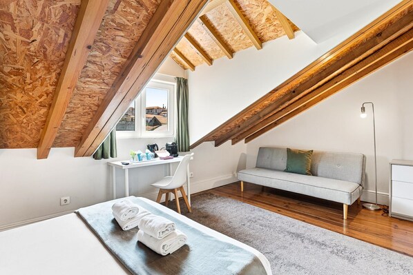 A loft bedroom with a sloped ceiling, a desk, a sofa, and a bed. - GuestReady - Porto Home V (Porto)