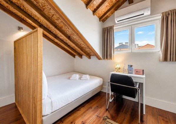 A single room with a bed, a desk, a chair, an air conditioning unit, and a window with curtains.