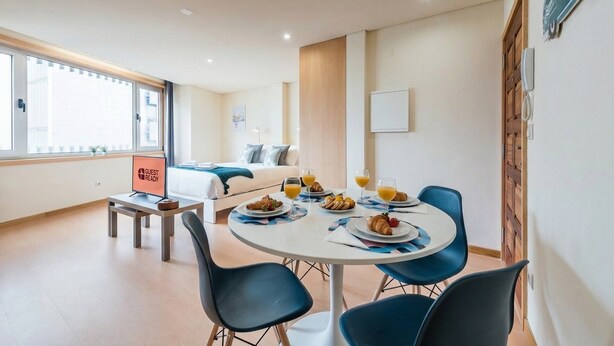 A modern hotel room with a bed, a dining table with breakfast, a desk, and a 'GUEST READY' sign.