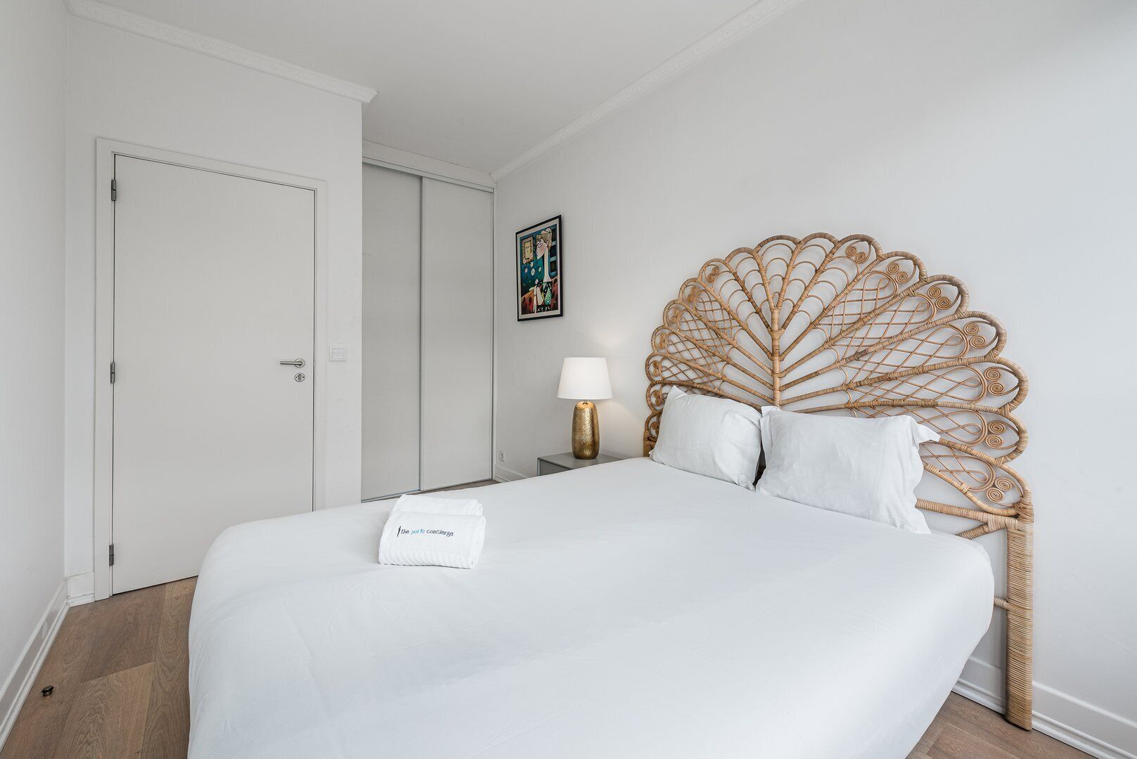 Une chambre d’hôtel avec un grand lit, une tête de lit en bois, une table de chevet avec une lampe et une porte.