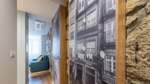 A hallway with a blue sofa, a stone wall, and a large black-and-white photo mural. - GuestReady - Crayon Walls Balcony (Porto)