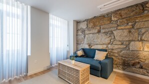 A living room with a stone wall, a blue sofa, and a woven coffee table. - GuestReady - Crayon Walls Balcony (Porto)