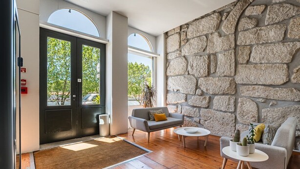 Un hall d’entrée moderne avec un mur en pierre, un canapé gris, une table basse et une porte donnant sur l’extérieur.