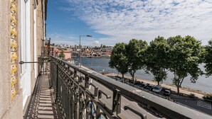 Un balcon avec une balustrade donnant sur une rivière, une vue sur la ville au loin et un ciel dégagé.